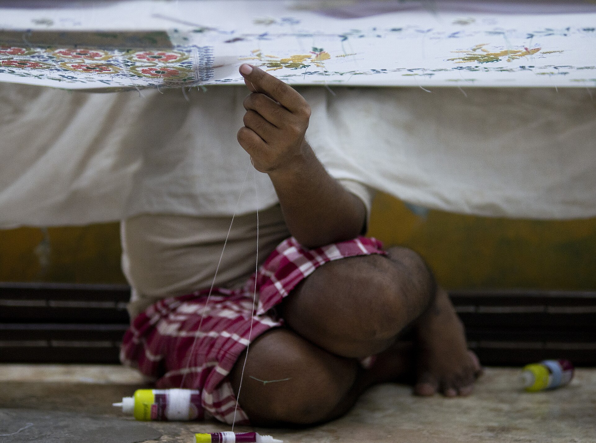 A zardozi artisan hand-embroidering a floral panel on a traditional frame in India